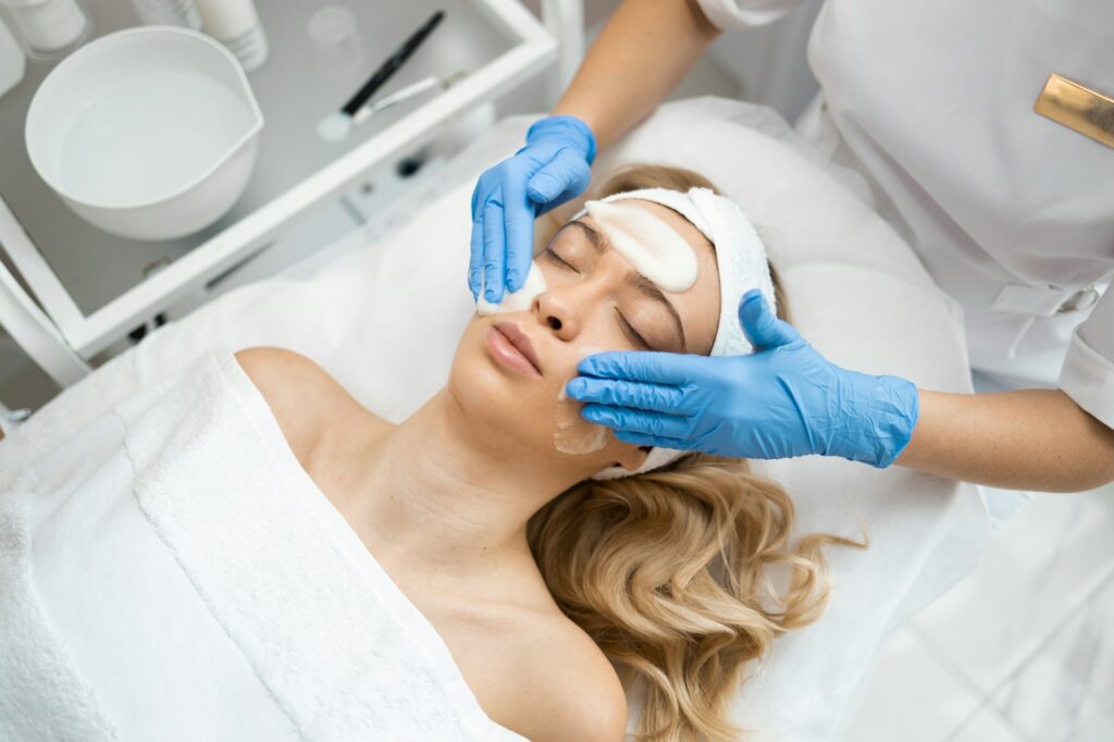 Dermatology doctor in gloves is applying facial cleansing foam on woman's face